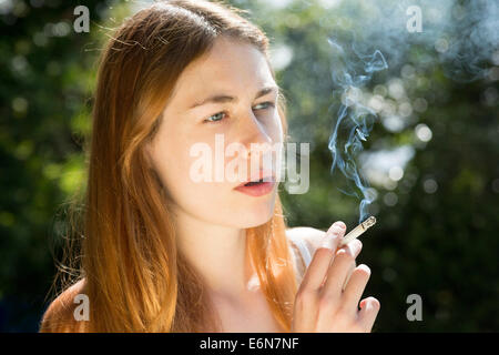 young woman smoking a cigarette outdoors Stock Photo