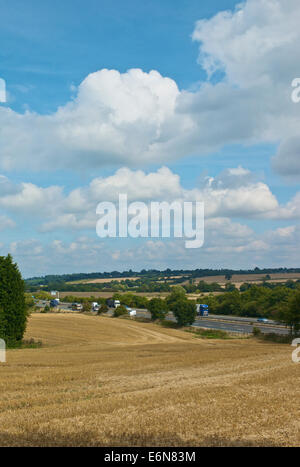 Traffic on M40 Motorway passing fields of recently cut crops and against bright blue sky background.