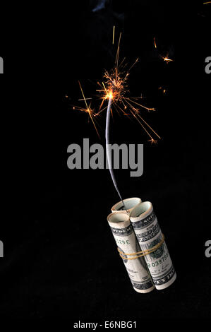 A roll of cash made into a dynamite stick has a lighted fuse throwing smoke and sparks before it explodes. Stock Photo