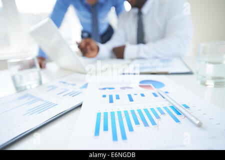 Documents with chart and graph and pen on background of two employees working Stock Photo