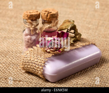 Spa background with purple soap, dried rose and glass bottles with sea salt and liquid. Stock Photo