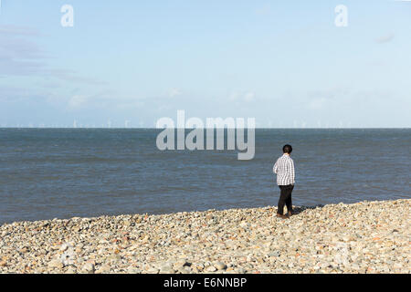 A teenage boy standing on the shingle beach at Llandudno, looking at the wind turbines of  Gwynt y Môr and Rhyl Flats wind farm. Stock Photo