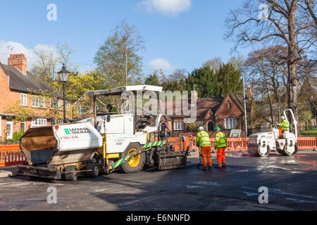 Road maintenance. Paver, road roller and road workers working on resurfacing roads in a village street, Nottinghamshire, England, UK Stock Photo