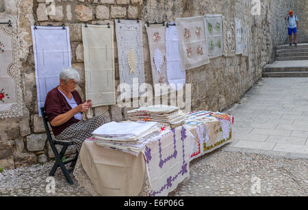 Elderly woman knitting table cloths and other knit wear in a side street of Dubrovnik old town. Stock Photo