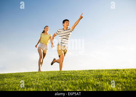 Cheerful young couple holding hands running on grass Stock Photo