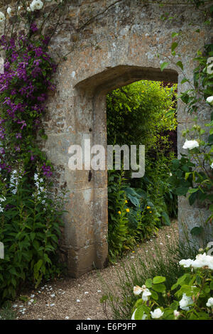 Framed by clematis and roses a stone archway links two parts of the walled garden of Rousham House in Oxfordshire, England Stock Photo