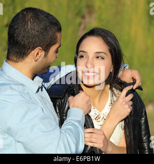 Happy arab couple flirting while gentleman cover her with his jacket in a park with a green background Stock Photo