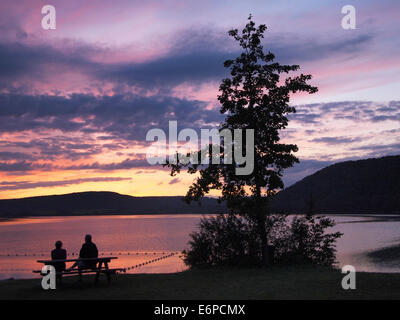 Lac de Chalain sunset, Jura, France with two silhouetted people sitting on a picnic table looking into the distance Stock Photo