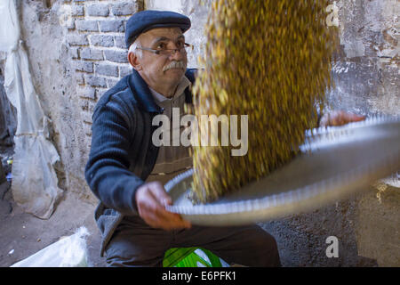 An old Iranian salesman sifting pistachio nuts in front of his shop in the old bazaar of Tabriz, Iran. Stock Photo