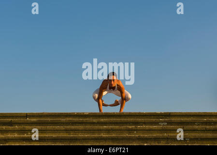 Young woman practising Hatha yoga, outdoors, showing the pose Kakasana, Bakasana, Crow pose, Crane pose Stock Photo