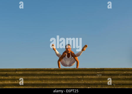 Young woman practising Hatha yoga, outdoors, showing the pose Kakasana, Bakasana, variation of Crow pose, Crane pose Stock Photo