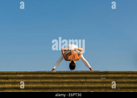 Young woman practising Hatha yoga, outdoors, showing the pose Prasarita padottanasana, Wide-legged forward bend Stock Photo