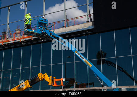 Dockland, Liverpool Waterfront, Merseyside, Construction is underway on the frontage of the new Kings Dock Exhibition Centre. Exterior cladding being affixed using 'Clad Boy' Vacuum Lifter device attached (taped) to JCB crane 540 170 with two workmen, fixing the cladding units,  using 'Easi-Lifts' extension bucket.  Liverpool in Work is supporting the main constructor contractor for the development, ISG Construction, with access to the local labour and subcontractor base, as well as support in filling in job vacancies and Apprenticeships. Stock Photo