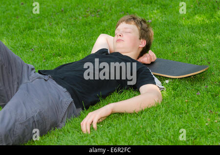 Teenager with skate resting or sleeps on the grass after active skateboarding Stock Photo