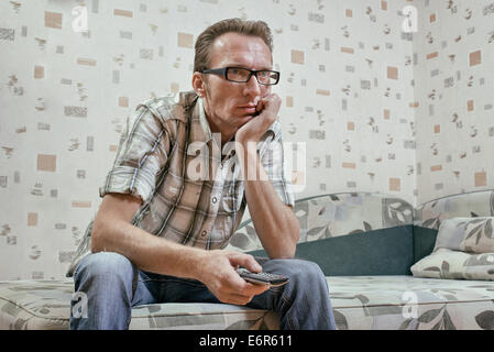 Sad and serious man with remote in his hand watch football maths or news broadcast on tv. Stock Photo