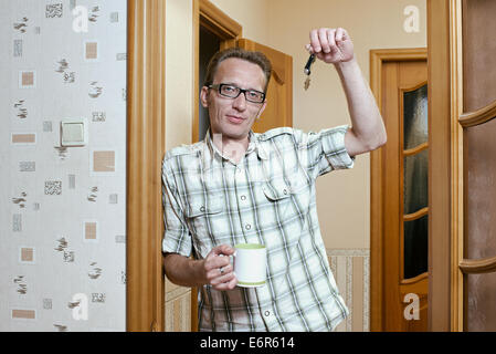 Man lean the doorpost and show the keys from the new apartment. Stock Photo