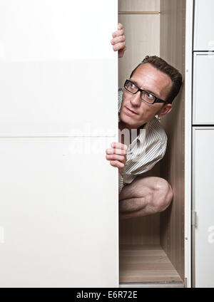 Prying man hiding inside white wardrobe. Stock Photo