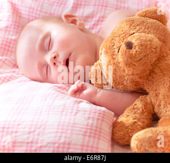 Portrait of adorable newborn baby sleeping on cute pink pillow with soft toy of teddy bear, day dreaming, love and childcare Stock Photo