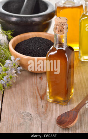 Nigella sativa oil in a bottle and nigella seeds and flowers on wooden background. Black cumin healing herb. Cold pressed. Stock Photo