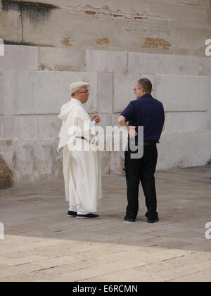 Man talking to clergyman wearing white robes in a street in Venice Stock Photo