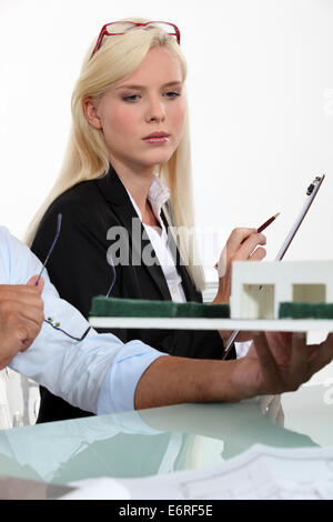 a blonde woman dressed in suit and a man looking a house scale model Stock Photo