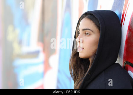 Profile portrait of a skater style teenager girl with an unfocused graffiti wall in the background Stock Photo