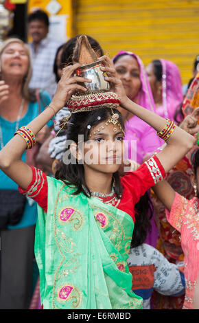 Pretty young girl in colourful clothes carrying a pot on her head in a wedding procession in Deogarh, Rajasthan, India Stock Photo