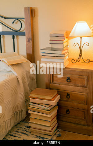 books stacked on a nightstand next to a bed Stock Photo