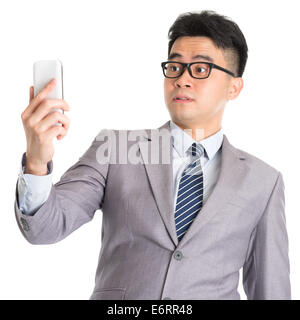 Asian business man with shocked facial expression while looking at smartphone, isolated on white background. Stock Photo