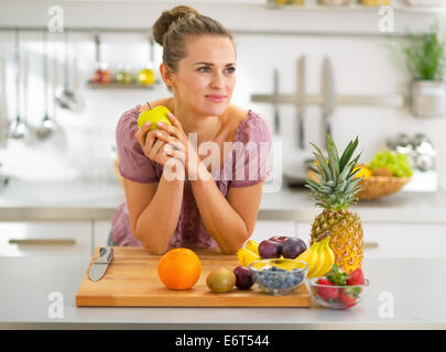 Portrait of thoughtful young housewife with fruits in modern kitchen Stock Photo