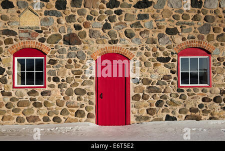 Old stone barn circa 1903.  Photo taken in winter.  Warm sunlight.  Bright red door and window frames with brick arches. Stock Photo