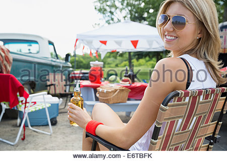 Woman drinking beer at tailgate barbecue in field