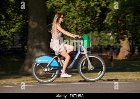 A woman cyclist on a public rental 'Boris bike' in a London park - London's public bicycle hire service, Hyde Park, London, UK Stock Photo