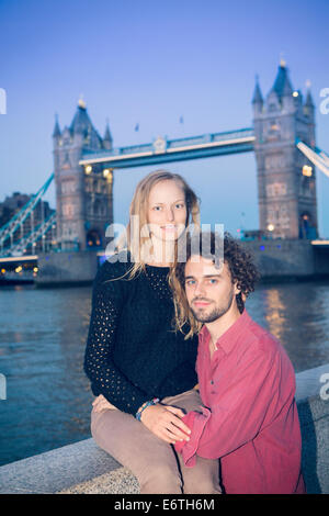 A young couple sitting in front of Tower Bridge, London Stock Photo