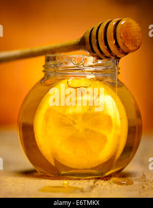 Glass jar of honey with wooden drizzler and slice of lemon on old wooden background. Stock Photo