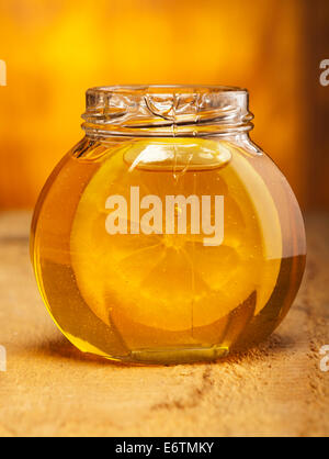 Glass jar of honey with slice of lemon on old wooden background. Stock Photo