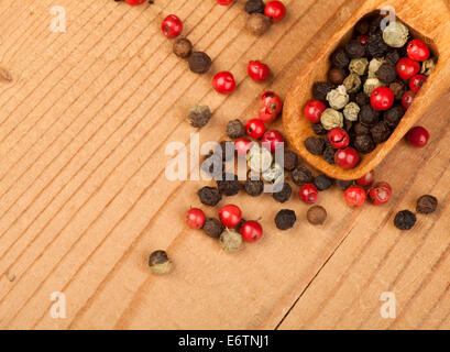 Three different kinds of peppercorns in wooden spoon on a wooden background. Stock Photo