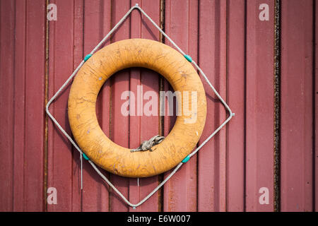 Old orange lifebuoy hanging on red wall Stock Photo