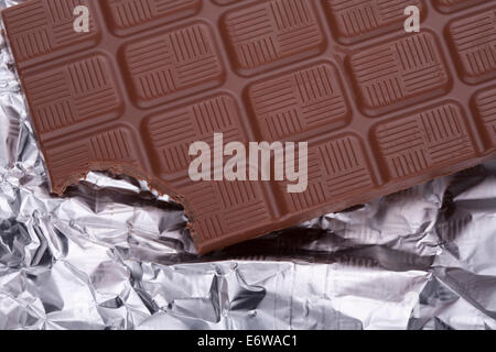 Bitten a piece of chocolate bar in silver foil packaging. Stock Photo