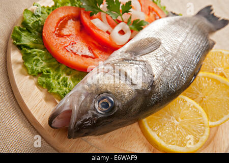 Freshly Bass Fish with vegetables on wooden cutting board. Stock Photo