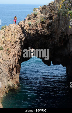 Young man jumping from the top of a natural arch on the Mediterranean coast. Théoule-sur-Mer, Esterel Massif, Alpes-Maritimes, French Riviera, France. Stock Photo