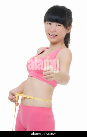 A very fit Asian woman measuring her waist and giving the Thumbs Up gesture isolated on a white background Stock Photo