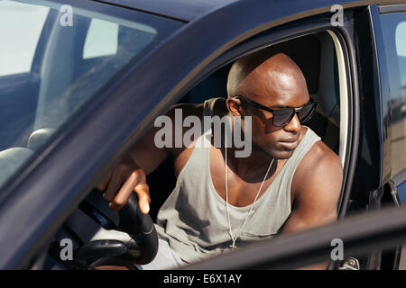 Image of young man in car looking away. Stylish African guy on road trip. Stock Photo
