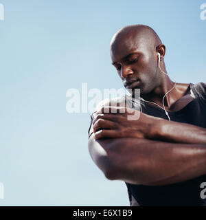 Low angle view African muscular man listening to music on mobile phone. Fit young man against sky. Stock Photo
