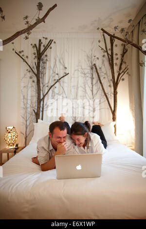 Young couple with laptop lying on a hotel bed, Milan, Lombardy, Italy Stock Photo