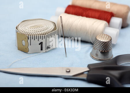 Sewing series. Tape measure, thimble, scissors and spool with needle on shirt. Closeup. Stock Photo