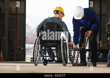 Maintenance supervisors one with spinal cord injury moving tow chain in utility truck garage Stock Photo