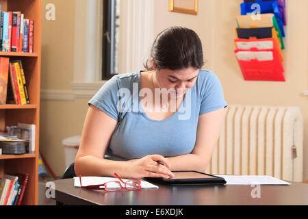 Woman with Asperger syndrome using her tablet to do work in home office Stock Photo