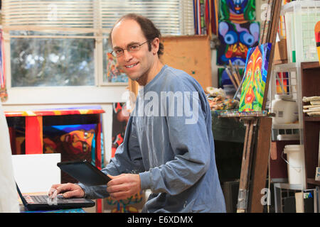 Man with Aspergers working on his tablet and computer in his art studio Stock Photo
