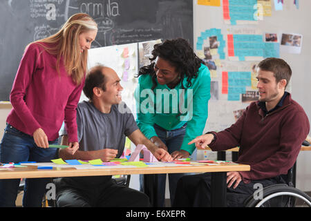 Engineering instructor demonstrating 3D shape to students in ideation lab one man with spinal cord injury and other one with Aspergers Stock Photo